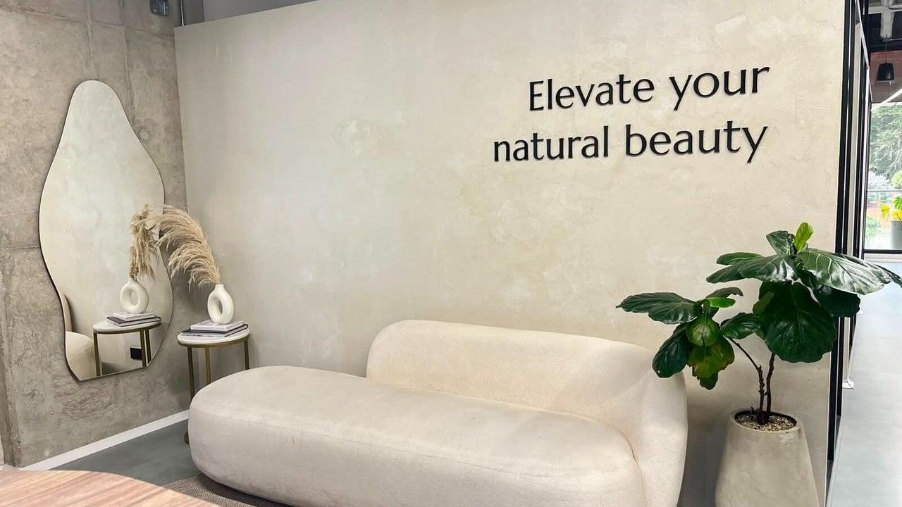 Sala de espera con sofá beige, espejo orgánico y la frase Elevate your natural beauty
